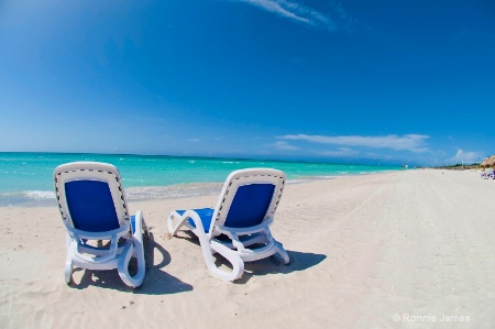Inviting water seen through a couple beach chairs 